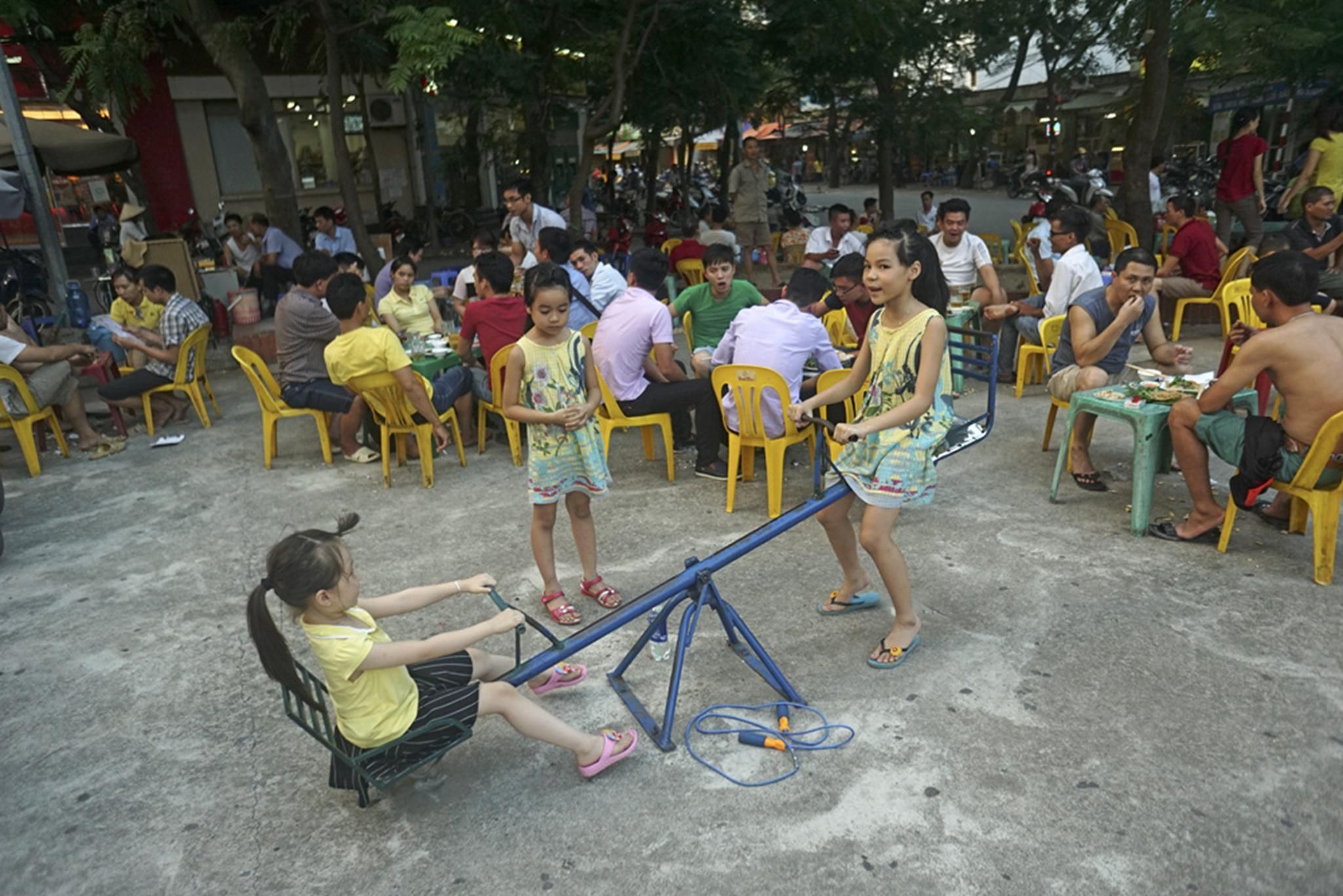 Những đứa trẻ chơi đùa bên cạnh những bàn nhậu ồn ào.